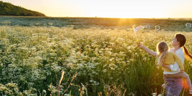 mom and daughter blowing bubbles in a field